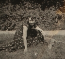"Olga Niewska, w letniej sukience, na polanie, obok leżącego koziołka."