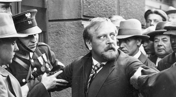  Bogusław Samborski jako kasjer Hieronim Śpiewankiewicz ( trzymany przez policjantów) w jednej ze scen filmu „Niebezpieczny romans”.  
